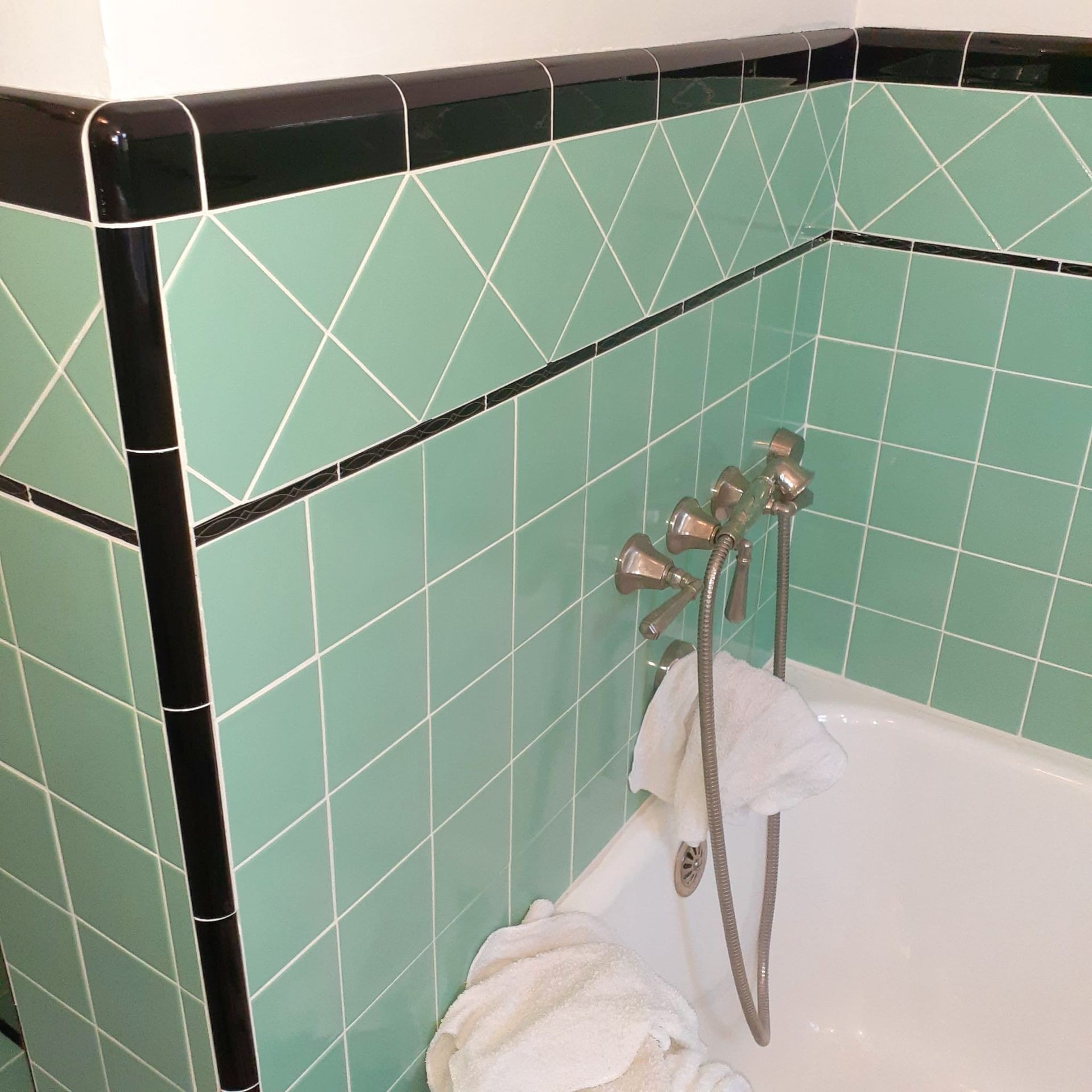 Bathroom corner with mint green and black tiled walls, bathtub faucet, and white towels.