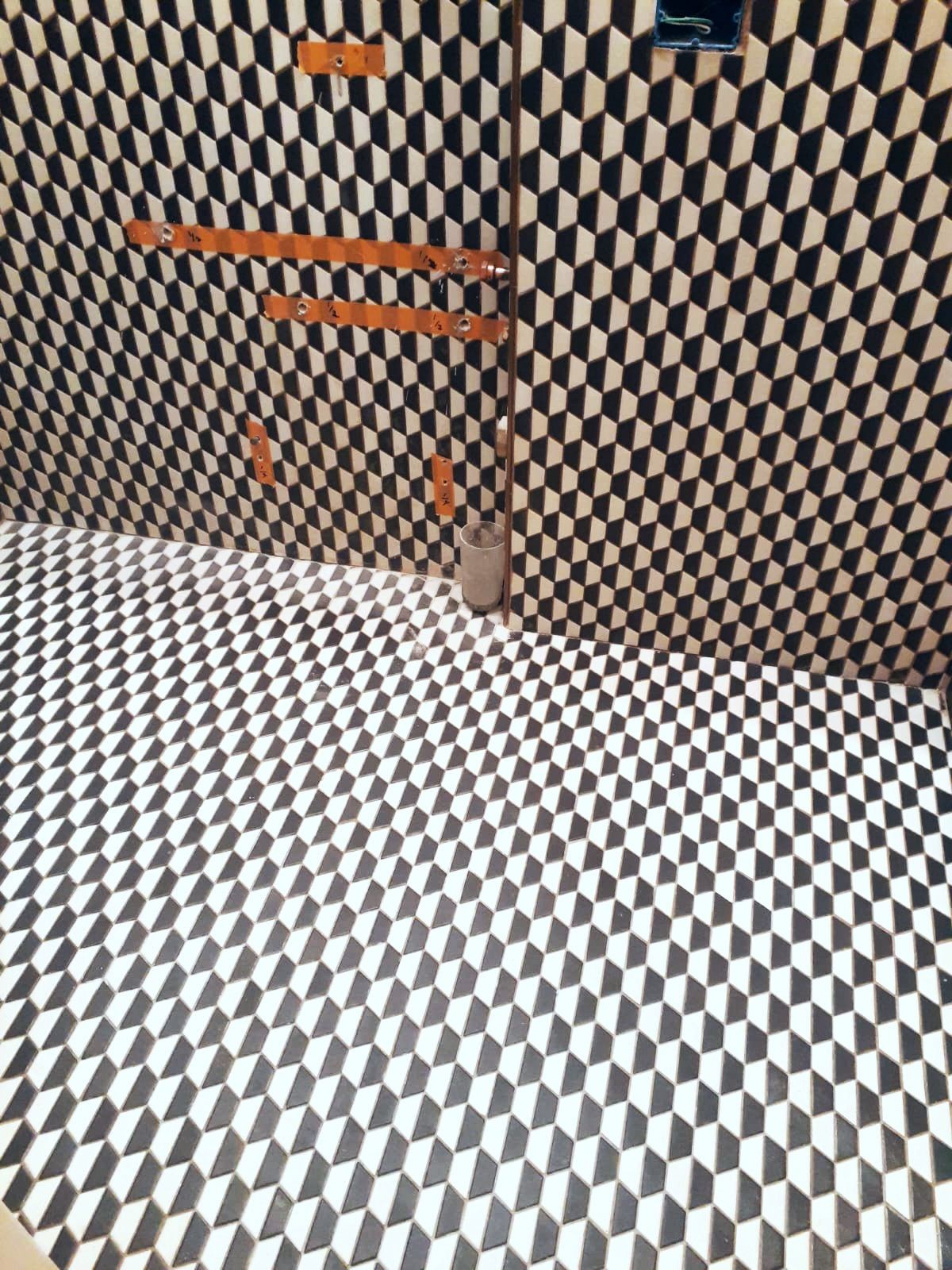 Room with black and white geometric patterned floor and walls, featuring exposed pipes and fittings.